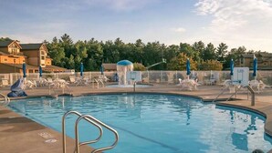 Une piscine entourée d’une clôture et d’arbres, avec des chaises longues et des parasols.