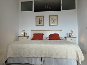 Un lit bien fait, recouvert d’une couverture à motifs, avec deux lampes de chevet et un cadre photo fixé au mur.