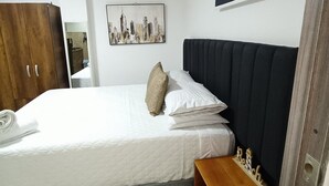Una camera da letto con un letto, un armadio in legno, un dipinto con una vista sulla città e una piccola mensola in legno.
