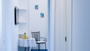 A narrow hallway with a blue tiled floor, a white door on the right, and a table with a chair in the center. - La Brezza Home (Piano di Sorrento)