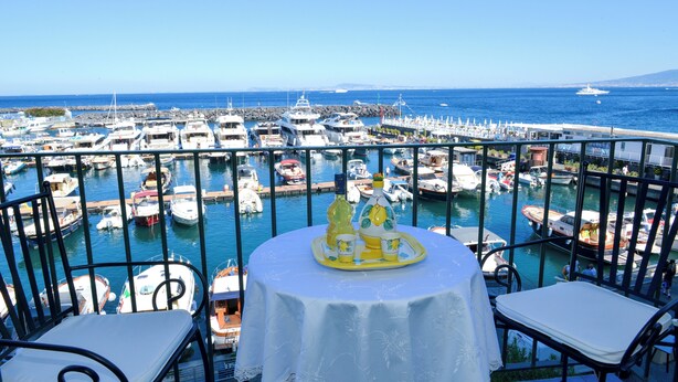 A balcony with a table set for two, overlooking a marina with various boats and yachts. - La Brezza Home (Piano di Sorrento)