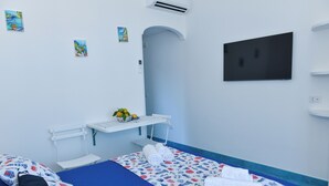 A hotel room with a bed, a TV, a small shelf with toiletries, and a wall-mounted air conditioner. - La Brezza Home (Piano di Sorrento)