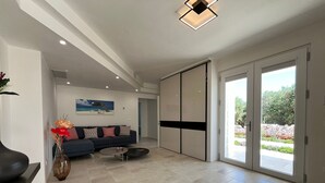 A spacious living room with a dark blue sofa, a coffee table, and a vase of flowers. There is a painting on the wall and a sliding glass door leading to an outdoor area. - Borgo Morgicchio (Carovigno)