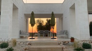 A modern outdoor seating area with two umbrellas, a stone pathway leading to the seating, and a view of the sunset in the background. - Borgo Morgicchio (Carovigno)