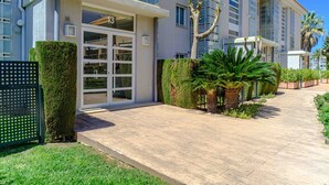 Ein modernes Hotel mit einer aufgeräumten Fassade, großen Fenstern und einem gepflegten Gartenbereich mit Palmen und ordentlich geschnittenen Hecken.