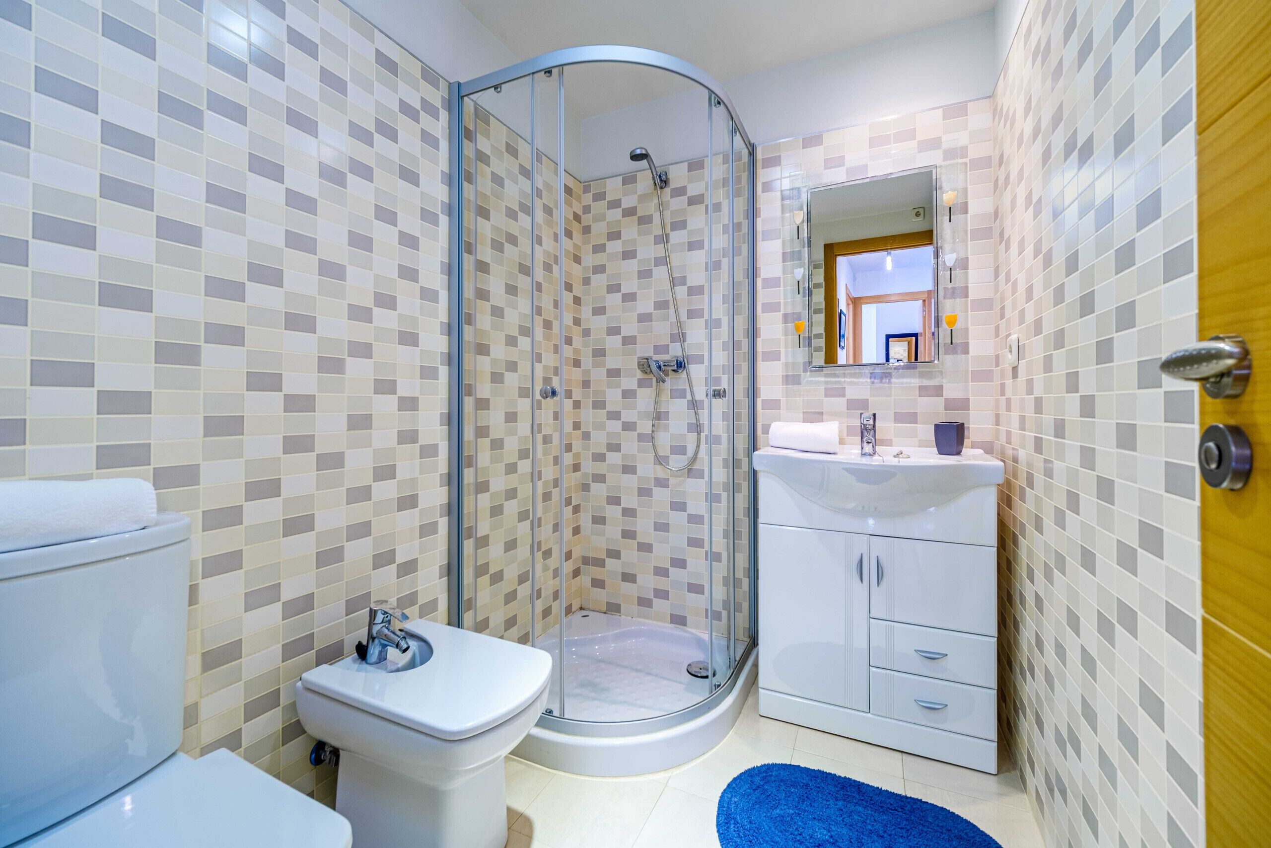 A bathroom with a glass-enclosed shower, a toilet, a sink, and a mirror.