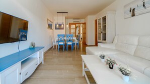 Ein modernes Wohnzimmer mit einem weißen Sofa, einer blauen Unterhaltungsecke und einem Essbereich mit blauen Stühlen.