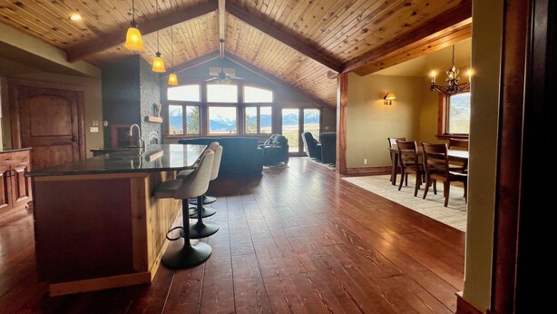 Une cuisine spacieuse avec un plafond en bois, un coin bar avec des tabourets et un espace repas avec une table et des chaises.