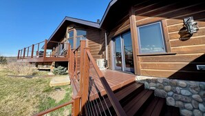 Une cabane en bois dotée d’une terrasse en bois, de fondations en pierre et d’une grande fenêtre.