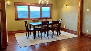 Un coin repas avec une table et des chaises en bois, un lustre et une fenêtre donnant sur le paysage.