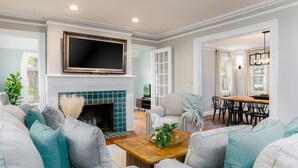 A modern living room with a fireplace, a television mounted above it, and a dining area with a table and chairs. - Discover university charm. Your 4-bedroom retreat, an 8-min drive to Notre Dame. (South Bend)