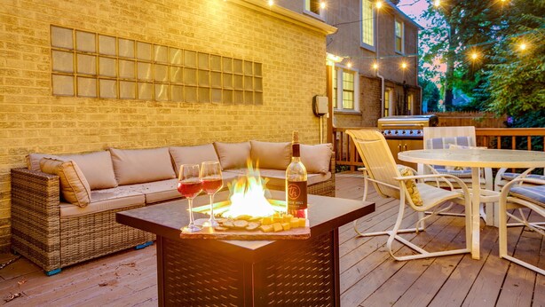 A wooden deck with a fire table, outdoor seating, and string lights. - Discover university charm. Your 4-bedroom retreat, an 8-min drive to Notre Dame. (South Bend)