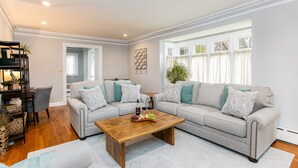 A living room with a sofa set, a coffee table with snacks, and a bookshelf. - Discover university charm. Your 4-bedroom retreat, an 8-min drive to Notre Dame. (South Bend)