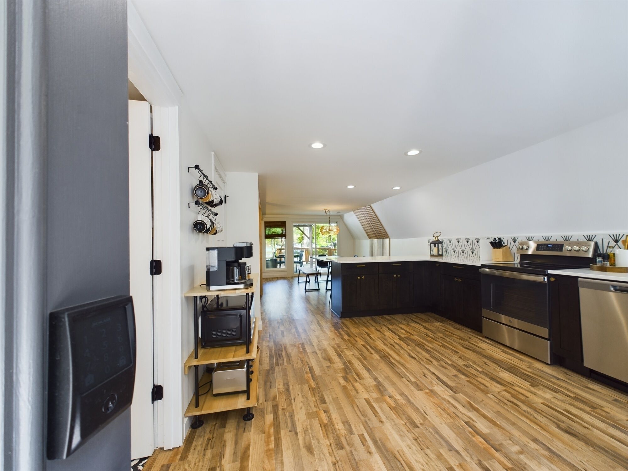 A modern kitchen with dark cabinets, stainless steel appliances, and a wooden floor.