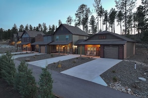 A row of modern houses with attached garages, a driveway, and a forested backdrop.