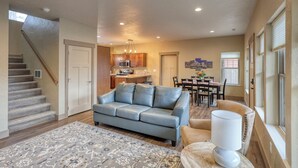 A spacious living area with a grey leather sofa, a patterned rug, and a dining table with chairs.