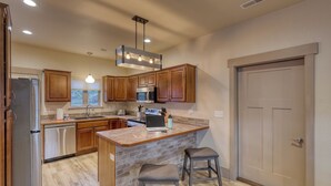 A modern kitchen with wooden cabinets, a granite countertop, a built-in island with stools, stainless steel appliances, and a pendant light. - Mt Rushmore Retreat hosted by Rockerville Gold Town Lodging • 8 Min Drive | 2 Bedroom Sleeps 6- Fireplace (Rockerville)