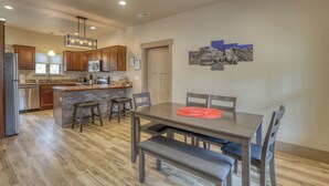 A modern kitchen with wooden cabinets, a central island, and a dining area with a bench and chairs. - Mt Rushmore Retreat hosted by Rockerville Gold Town Lodging • 8 Min Drive | 2 Bedroom Sleeps 6- Fireplace (Rockerville)