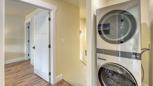 Un cuarto de lavado con lavadora y secadora de carga frontal, una puerta que da a otra habitación y un interruptor de luz en la pared.