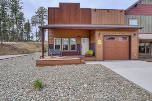 A two-story building with a garage, a bench, and a planter on the front porch.