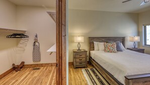 Un dormitorio con cabecera de madera, cama con muchos almohadones, dos mesitas de noche con lámparas, suelo de madera y una ventana con luz natural.