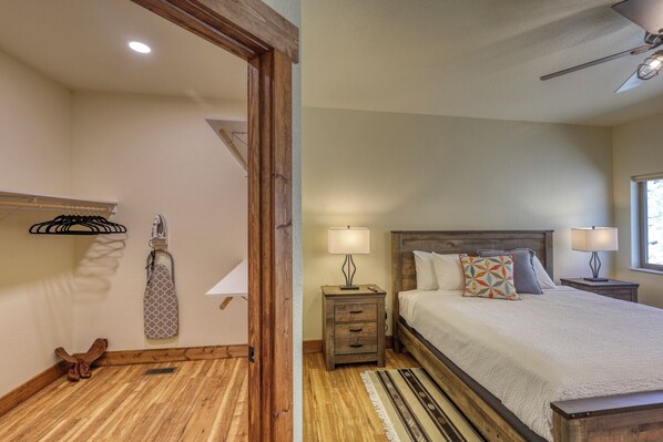 A bedroom with a wooden headboard, a bed with multiple pillows, two bedside tables with lamps, a wooden floor, and a window with natural light.