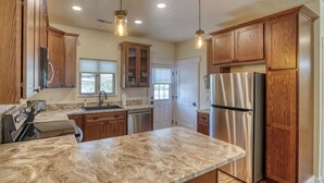 A kitchen with wooden cabinets, a stainless steel refrigerator, and a marble countertop. - Homestake Haven Hosted by Rockerville Gold Town Lodging-Black Hills Base Camp-2 Bedroom, King Suite (Rockerville)