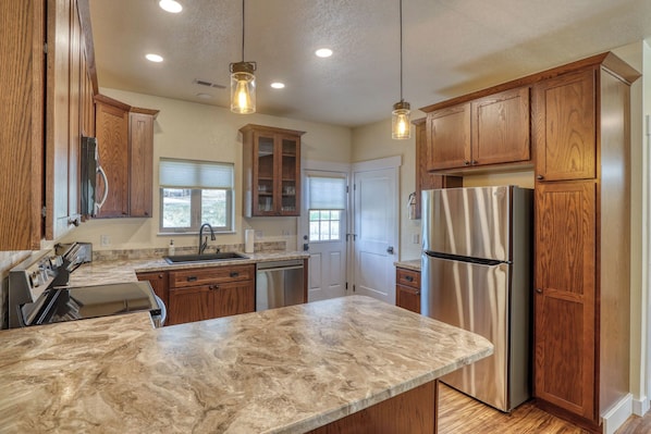 A kitchen with wooden cabinets, a stainless steel refrigerator, and a marble countertop.