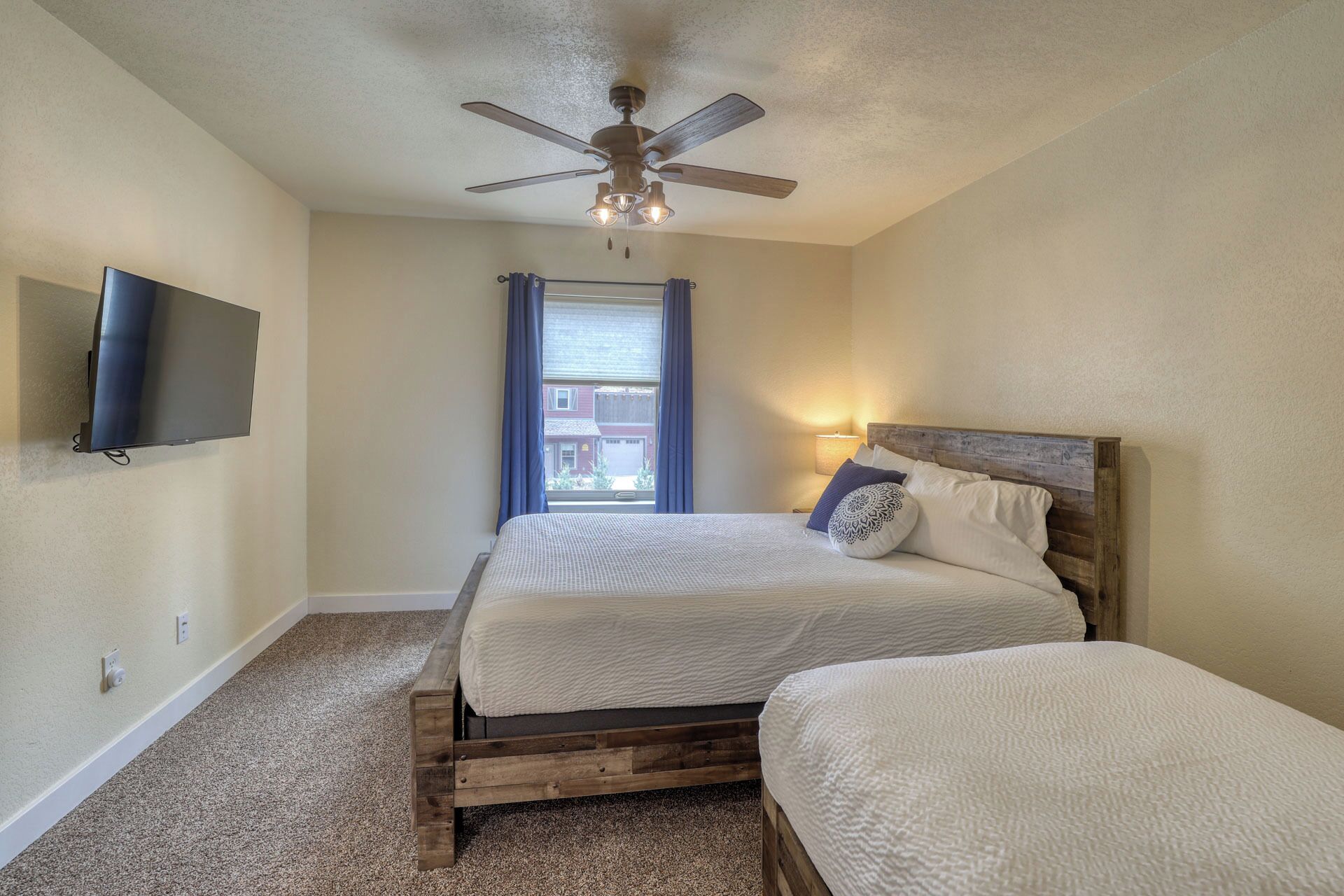 A bedroom with a bed, a ceiling fan, a TV, and a window with curtains.