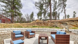 Outdoor wicker furniture with cushions, a stone wall, and a forested hillside. - Homestake Haven Hosted by Rockerville Gold Town Lodging-Black Hills Base Camp-2 Bedroom, King Suite (Rockerville)