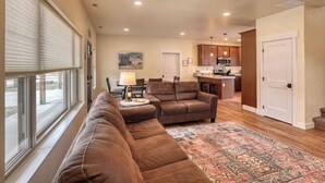 A living room with a brown sofa, a dining area with chairs, a kitchen with wooden cabinets, and a patterned rug. - Homestake Haven Hosted by Rockerville Gold Town Lodging-Black Hills Base Camp-2 Bedroom, King Suite (Rockerville)