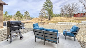 Eine Terrasse mit Grill, zwei blaue Sitzgelegenheiten mit Polstern und einer Steinmauer.