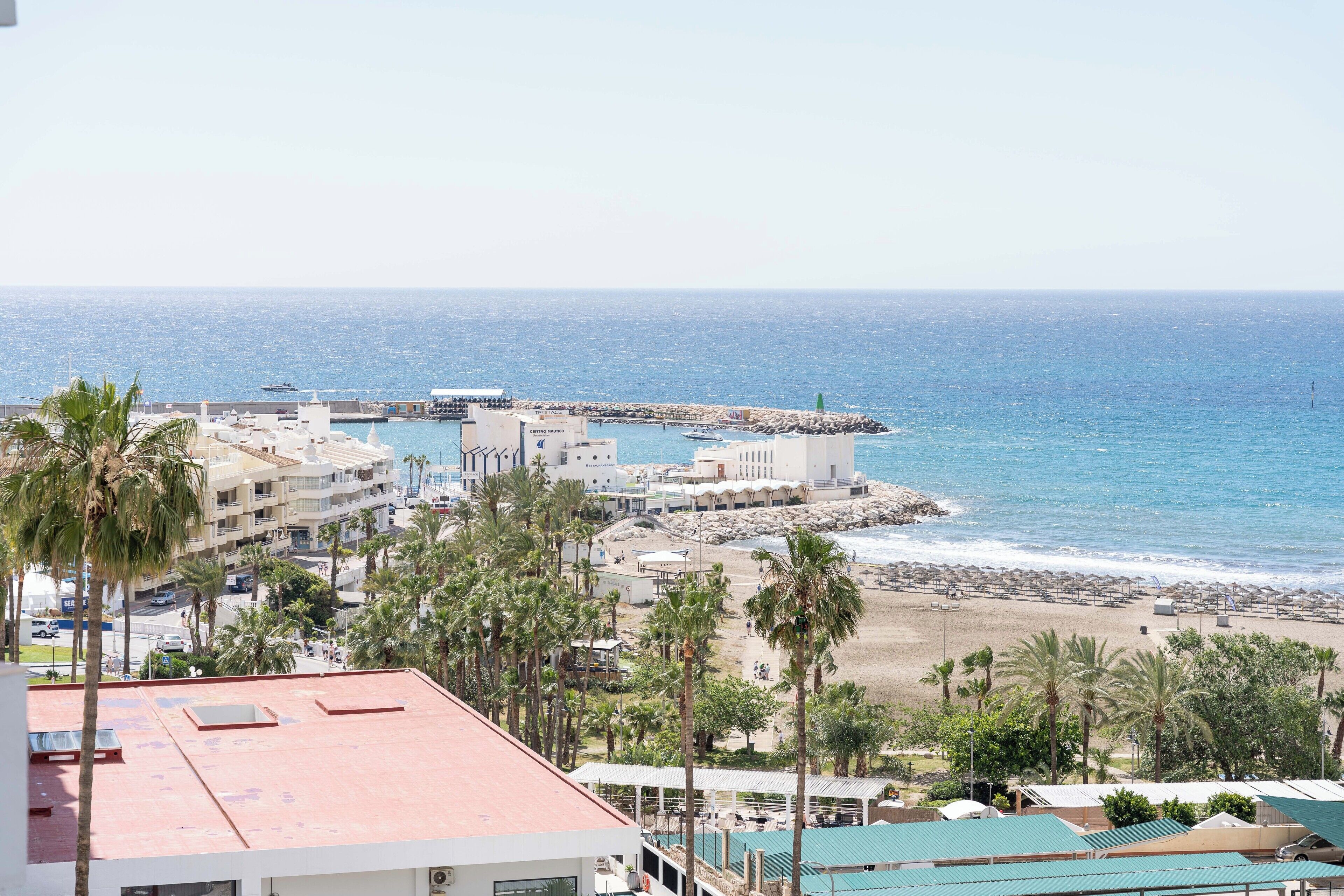 Un hotel costero con varios pisos, vista a la playa y un muelle rocoso.