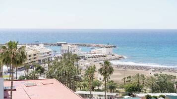 Un hotel costero con varios pisos, vista a la playa y un muelle rocoso.