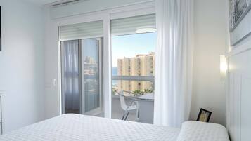 Un dormitorio con una cama grande, una puerta corrediza de vidrio que da a un balcón y vistas a edificios a lo lejos.
