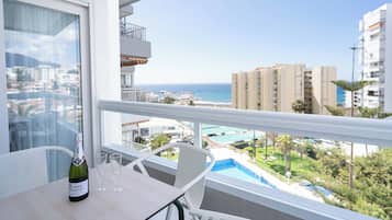 Un balcón con vistas al mar y edificios, una botella de champán y dos copas sobre una mesa.