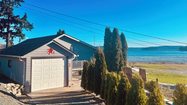 A house with a garage, a driveway leading to the garage, and a view of the ocean. - Similk Beach View Studio for two! 
Central HUB to San Juans and Skagit Valley! (Anacortes)