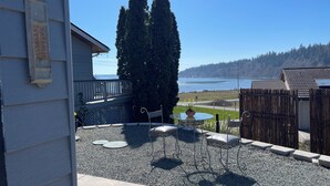 A patio with a table and chairs, a potted plant, and a view of a lake. - Similk Beach View Studio for two! 
Central HUB to San Juans and Skagit Valley! (Anacortes)