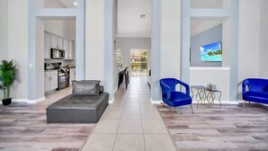 A spacious living area with a sofa, blue chairs, a small table, and a TV displaying a beach scene. - Newly Remodeled Disney Vacation Home (Davenport)
