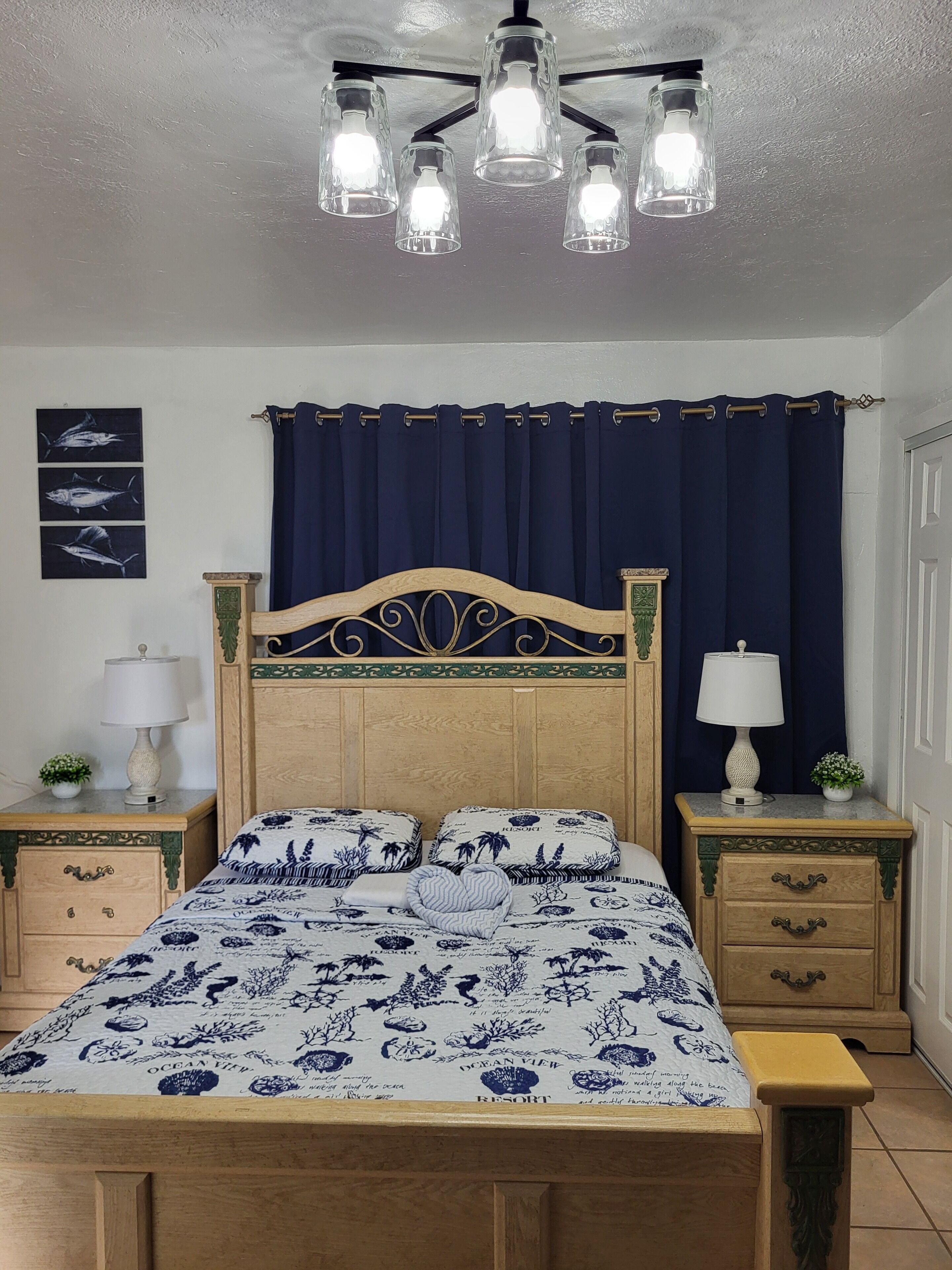 A bedroom with a wooden bed, a nightstand with a lamp, a decorative headboard, and a ceiling light fixture.