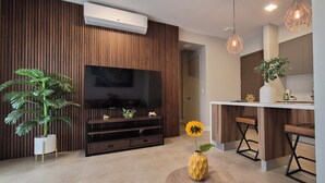 Een moderne woonkamer met een flatscreen televisie, houten paneelwanden, een grote potplant, een ronde tafel met een vaas, en een bar met barkrukken.