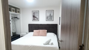 A bedroom with a bed, a nightstand, a wardrobe, and two framed pictures on the wall.