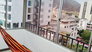 A balcony with a hammock, large windows, and a view of buildings and mountains.