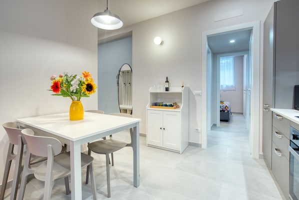 A modern kitchen with white cabinets, a dining area with a white table and chairs, and a vase of flowers on the table.