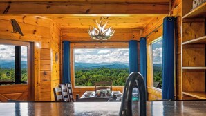 L’intérieur d’un chalet en bois comprend un coin repas, un évier et offre une vue sur une chaîne de montagnes boisée.