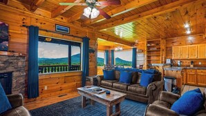 Un intérieur de chalet chaleureux avec une cheminée en pierre, des murs en bois, un coin repas et une vue sur les montagnes.