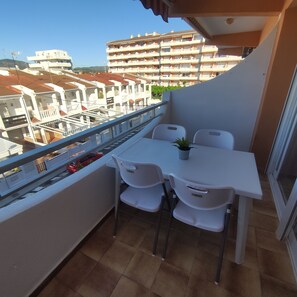 Un balcon avec une table et des chaises, un pot de fleurs et une vue sur les bâtiments en arrière-plan.