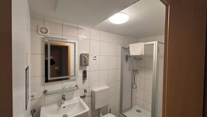 Un baño con lavamanos, inodoro, espejo y ducha con mampara de vidrio.