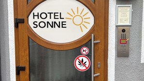 Puerta de hotel con un cartel que dice 'HOTEL SONNE', un símbolo de sol y un letrero de 'No fumar'.