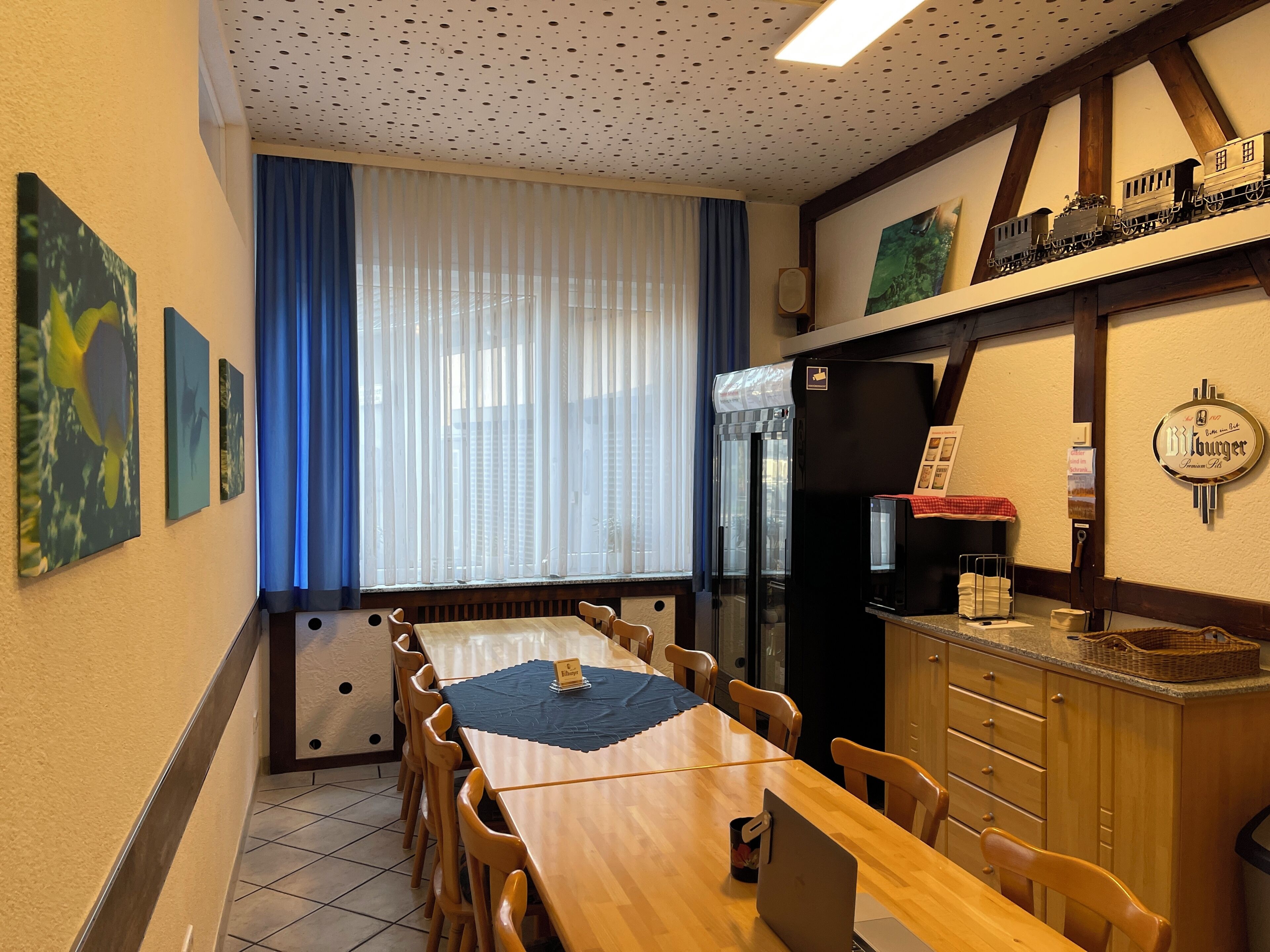 Ein Essbereich mit einem langen Holztisch, Stühlen, einem Kühlschrank, einer Zapfsäule für Bier und Kunstwerken an den Wänden.